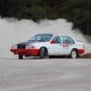 En rallybil sneddar genom en kurva, bakom bilen är ett stort dammoln.