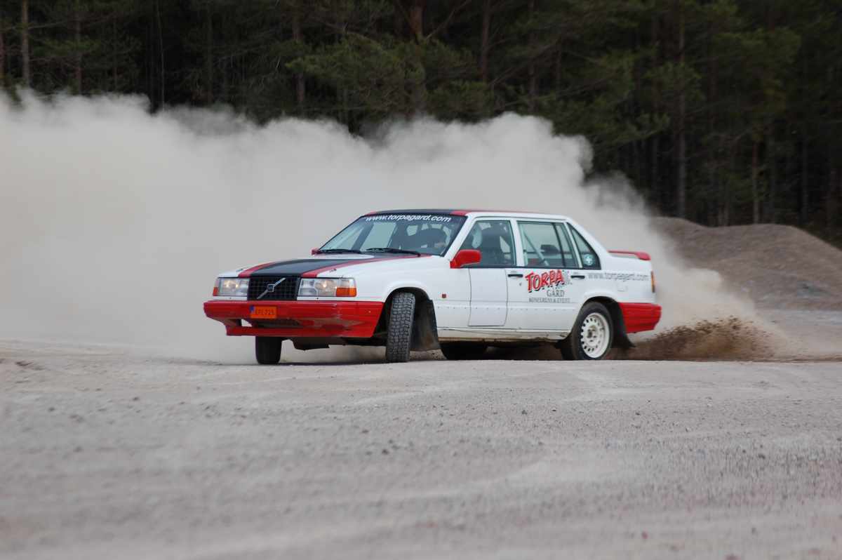 En rallybil sneddar genom en kurva, bakom bilen är ett stort dammoln.