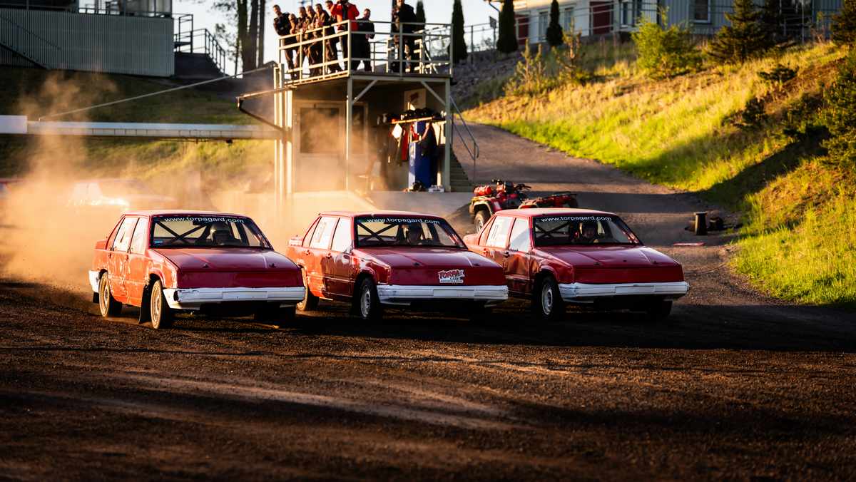 Tre röda, smutsiga folkrace-bilar ligger nästan jämsides på en grus-motorbana.
